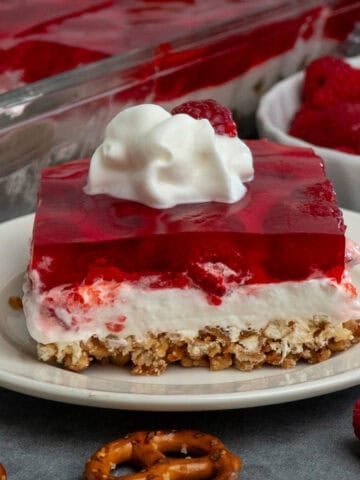 Raspberry pretzel salad on a plate and topped with whipped cream.