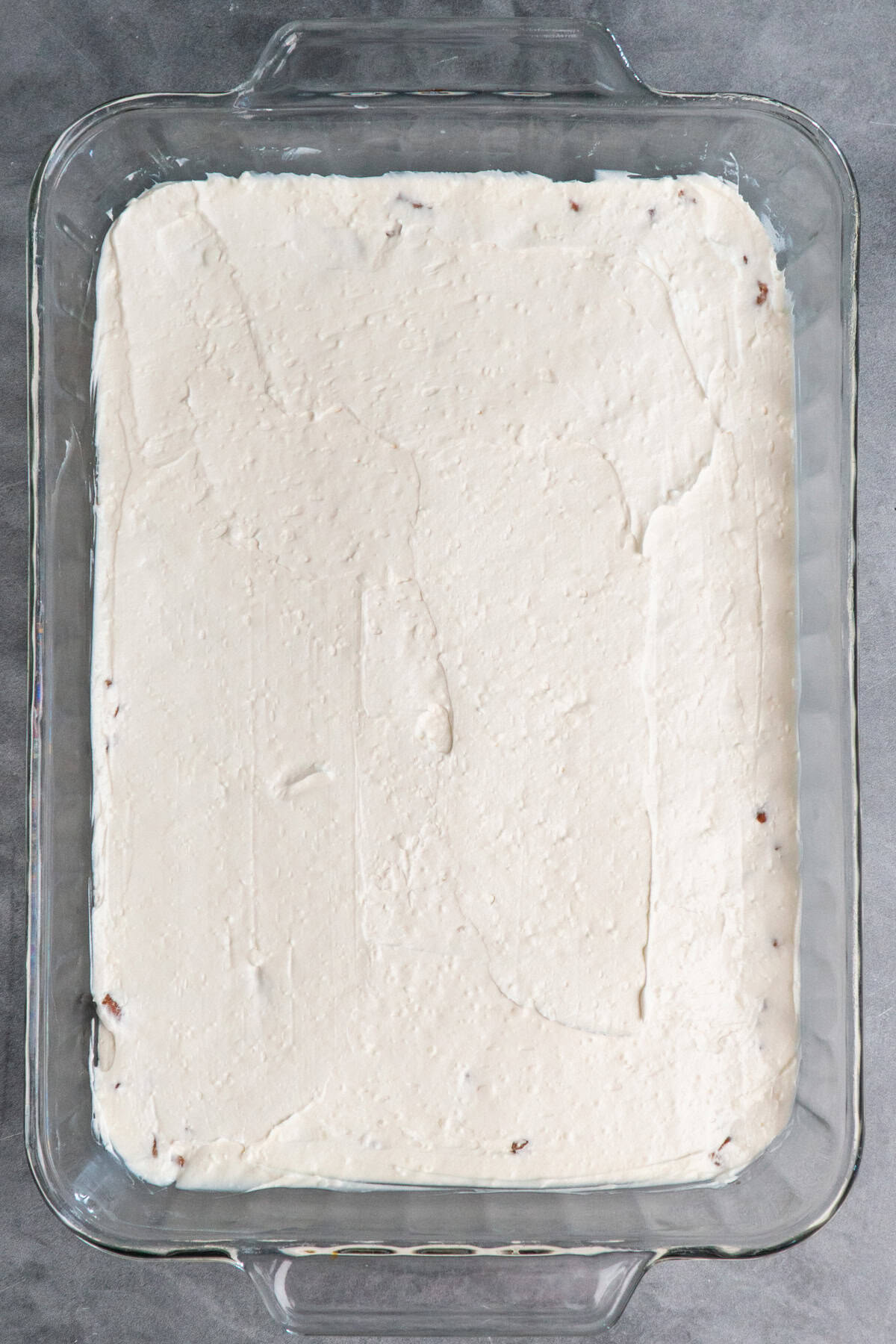 Cream cheese mixture spread over pretzel crust in a clear baking dish.