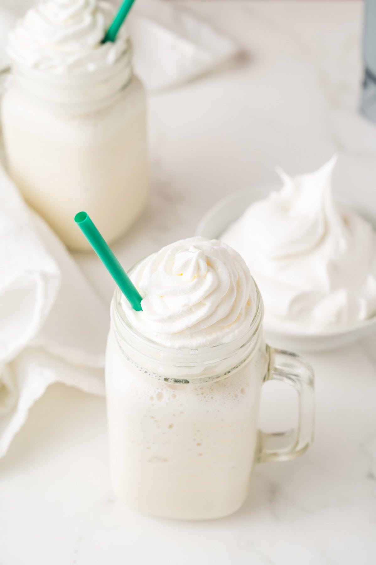 A vanilla frappuccino blended and added to a glass with whipped cream and a straw.