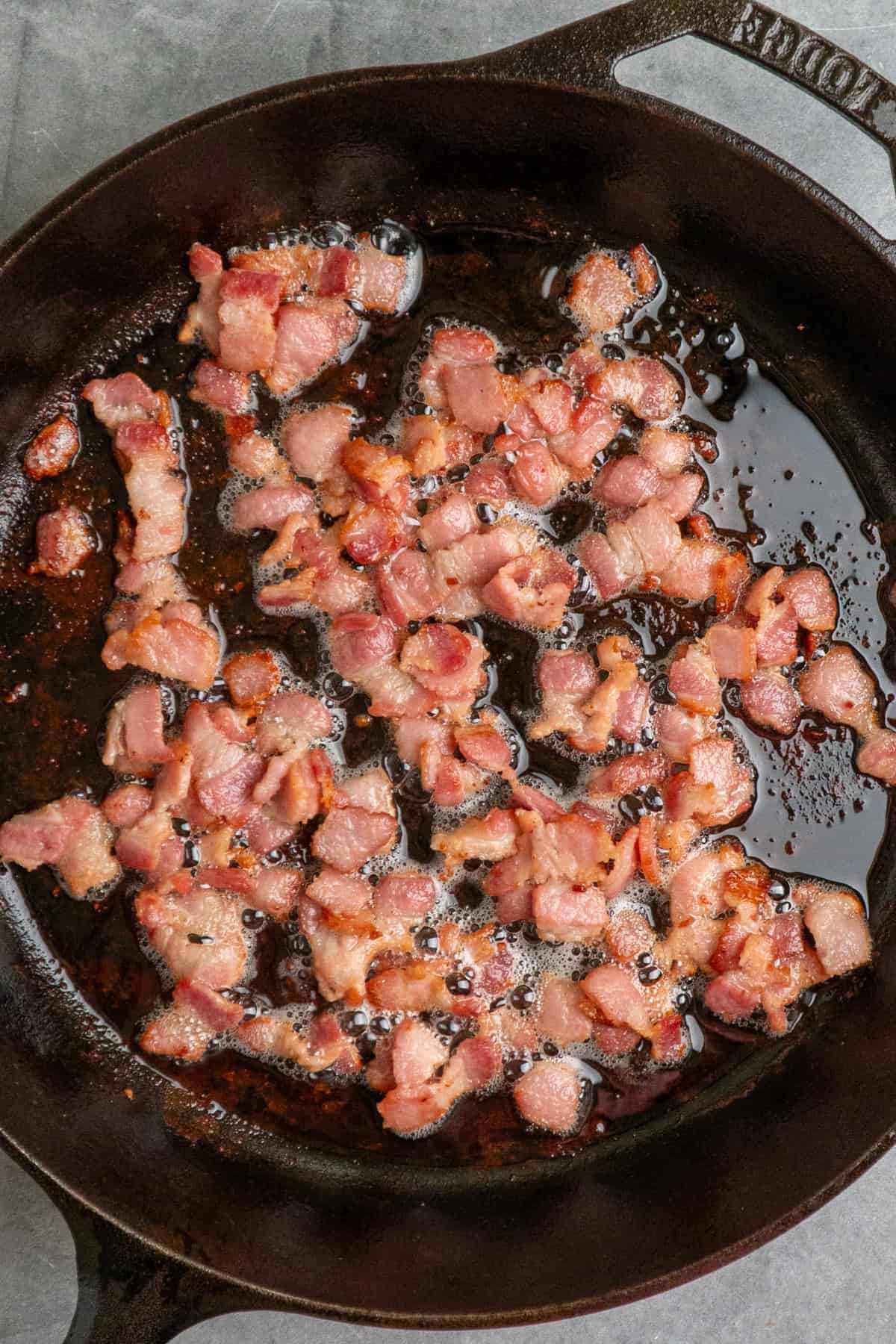 Chopped bacon cooking in a cast iron skillet.