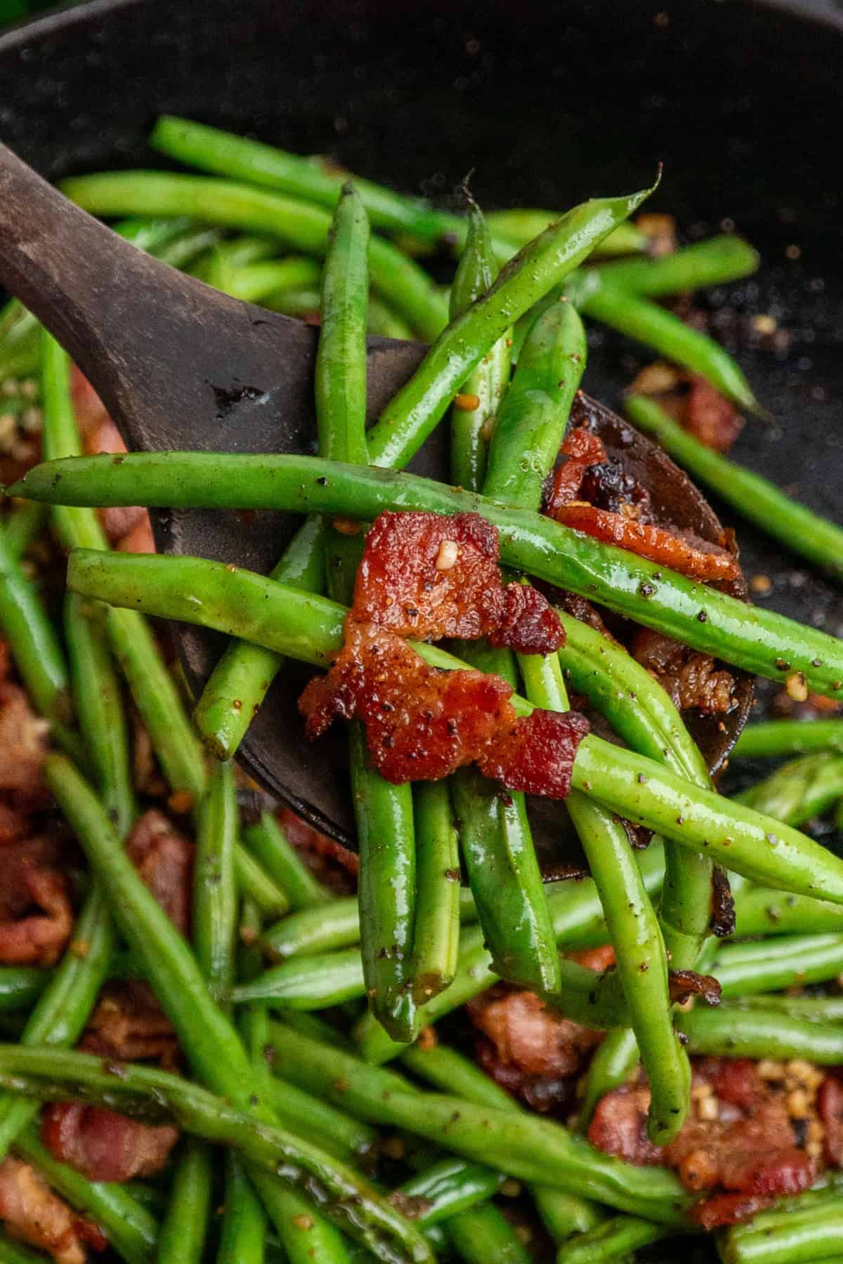 A wooden spoon holding a serving of green beans with bacon.