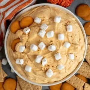 Pumpkin fluff dip in a white bowl with nilla wafers and graham crackers around it.