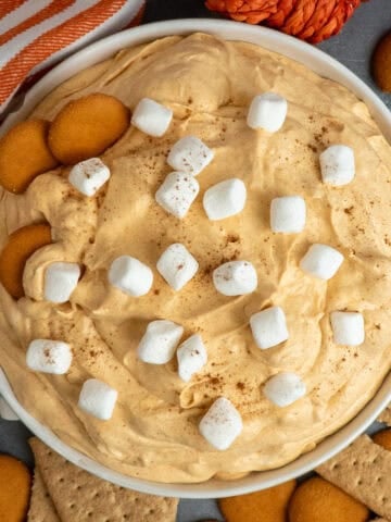 Pumpkin fluff dip in a white bowl with nilla wafers and graham crackers around it.