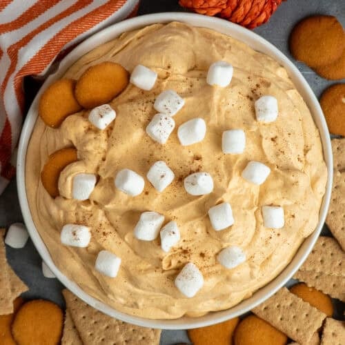Pumpkin fluff dip in a white bowl with nilla wafers and graham crackers around it.