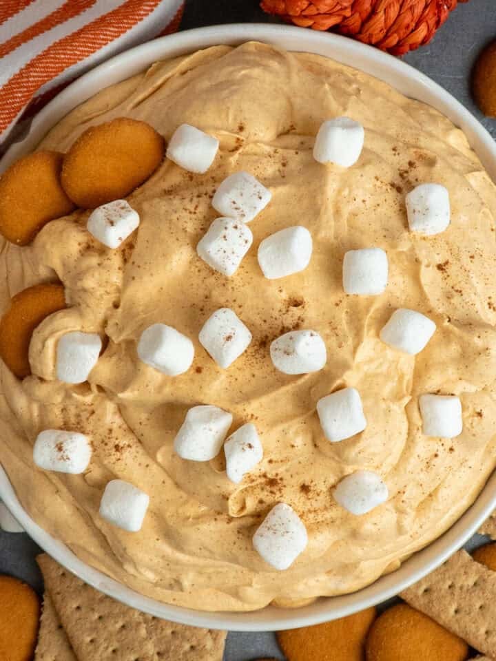 Pumpkin fluff dip in a white bowl with nilla wafers and graham crackers around it.