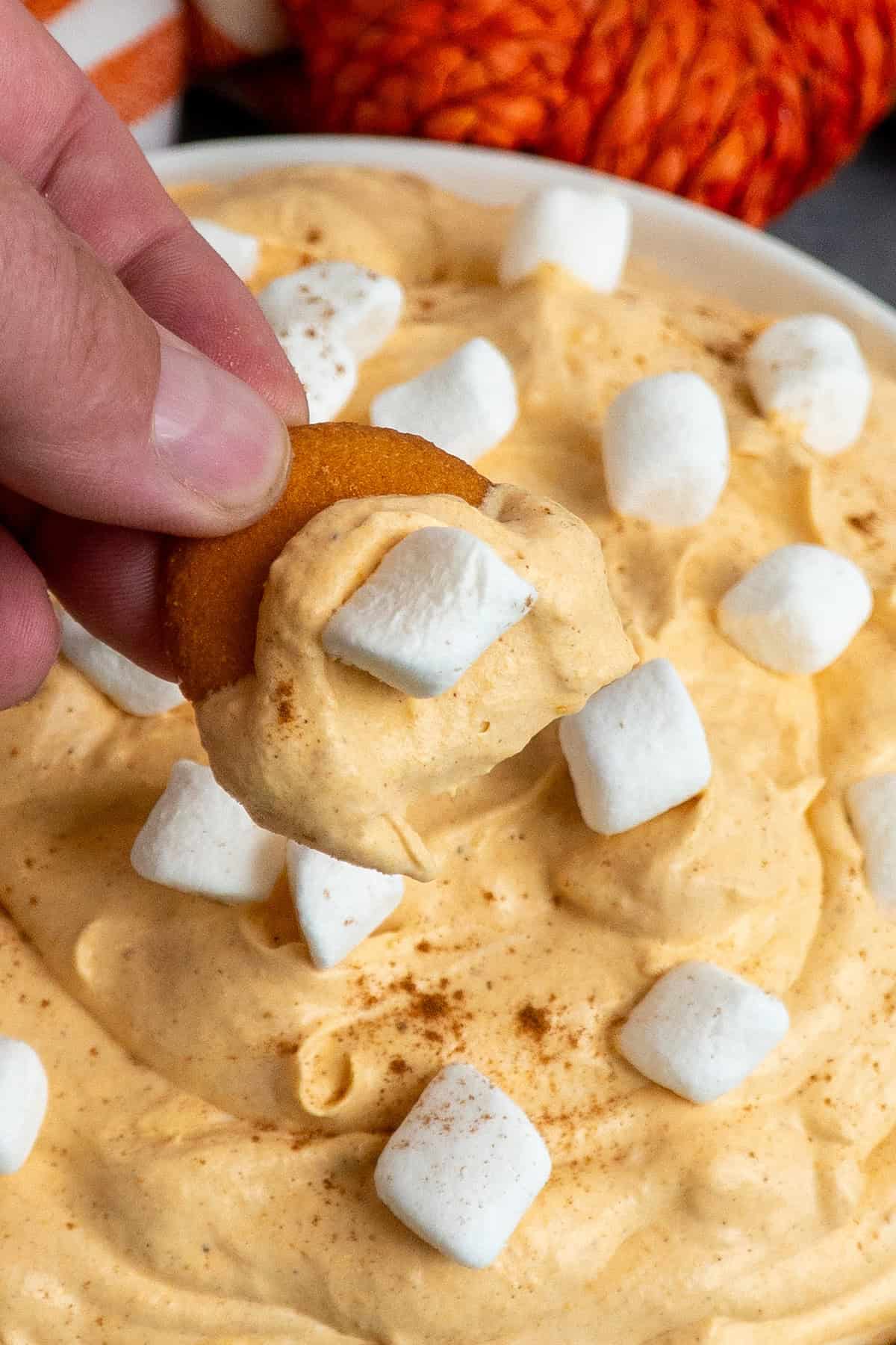A hand holding a bite of pumpkin fluff dip on a cookie.