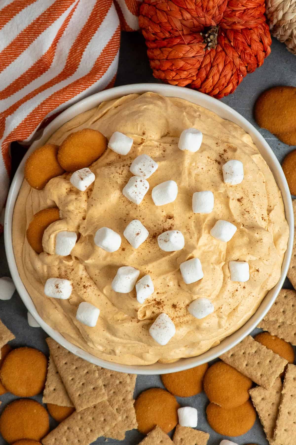 Pumpkin fluff dip in a white bowl with nilla wafers and graham crackers around it.