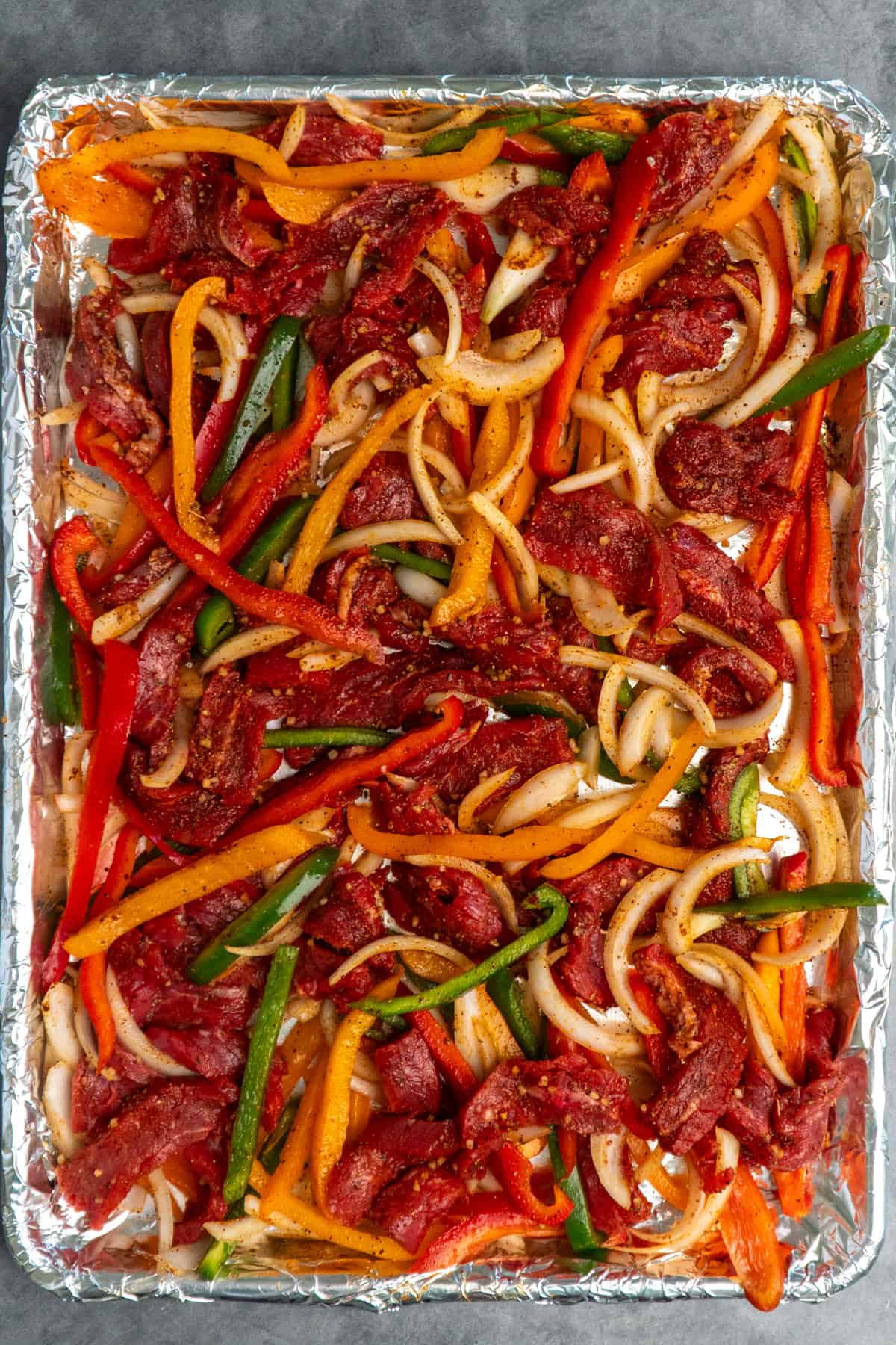 Sliced bell peppers, onion and steak on a sheet pan.