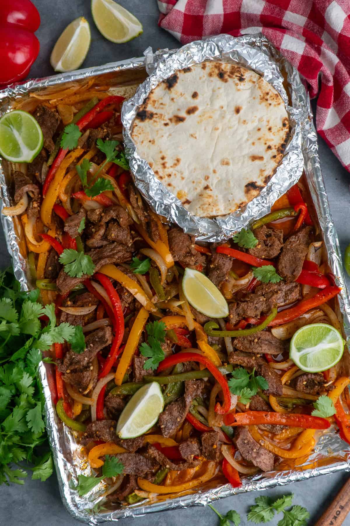 Sheet pan steak fajitas with tortillas and lime.