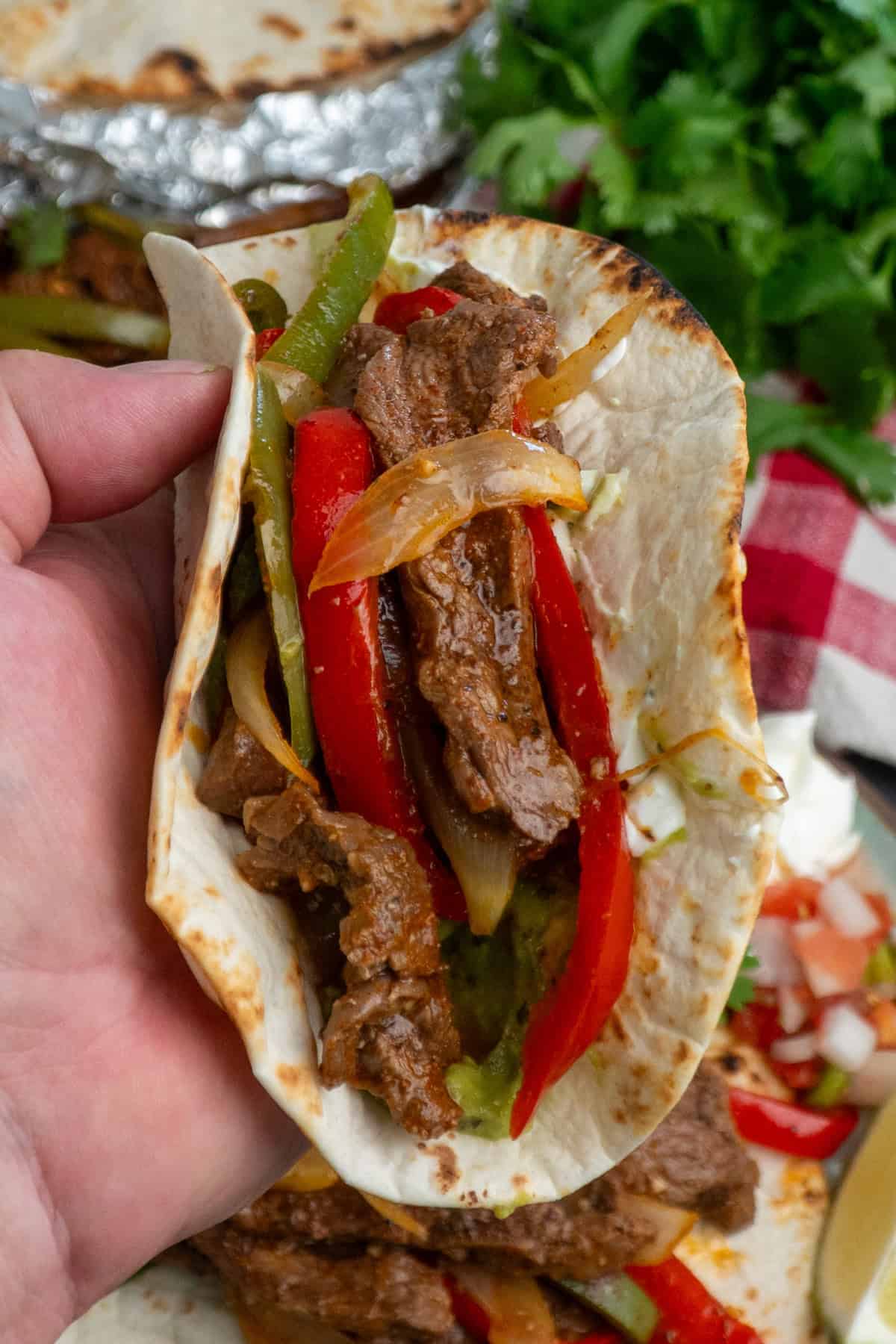 A fajita with steak, peppers and onions being held up.