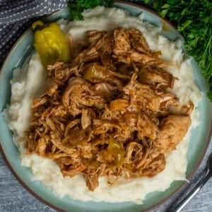 Crock Pot Mississippi chicken over a plate of mashed potatoes.