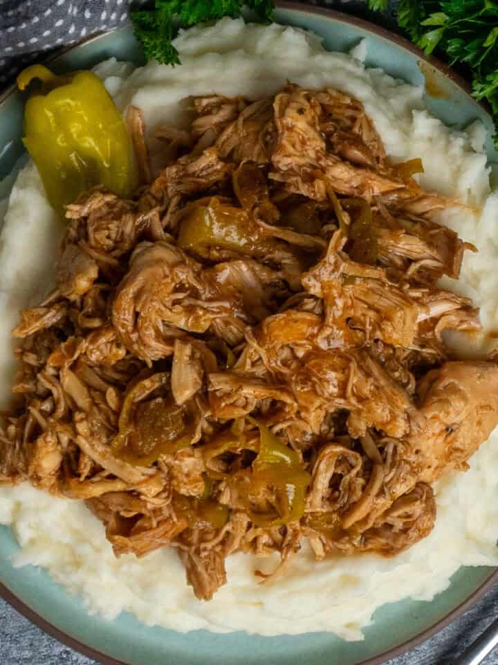 Crock Pot Mississippi chicken over a plate of mashed potatoes.