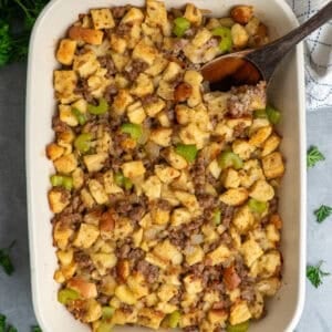 Sausage stuffing in a baking dish with a wooden spoon.