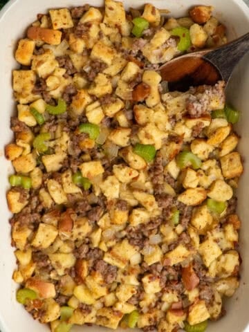 Sausage stuffing in a baking dish with a wooden spoon.