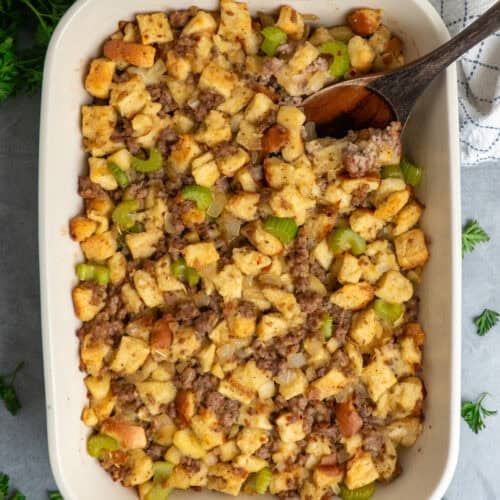 Sausage stuffing in a baking dish with a wooden spoon.