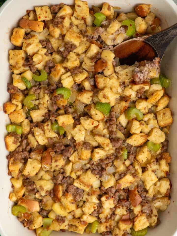 Sausage stuffing in a baking dish with a wooden spoon.