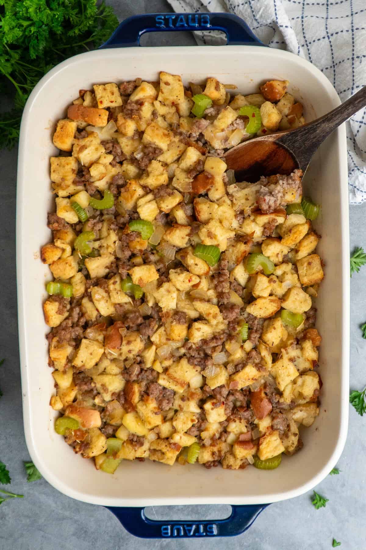Sausage stuffing in a baking dish with a wooden spoon.