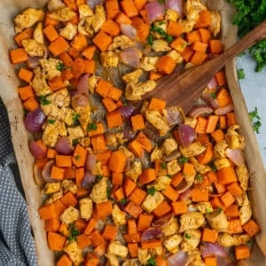 Sheet pan chicken and sweet potatoes with a wooden spatula ready to be served.