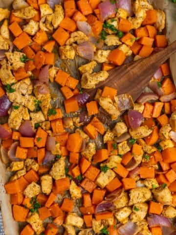 Sheet pan chicken and sweet potatoes with a wooden spatula ready to be served.