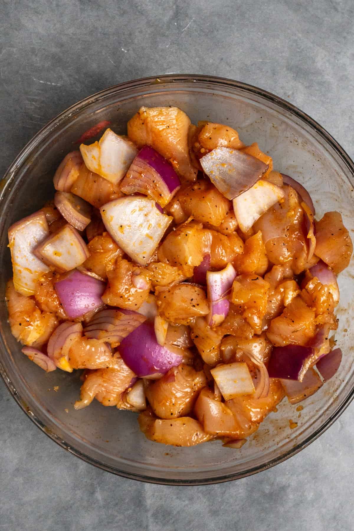 Chicken and onions marinading in a clear bowl.
