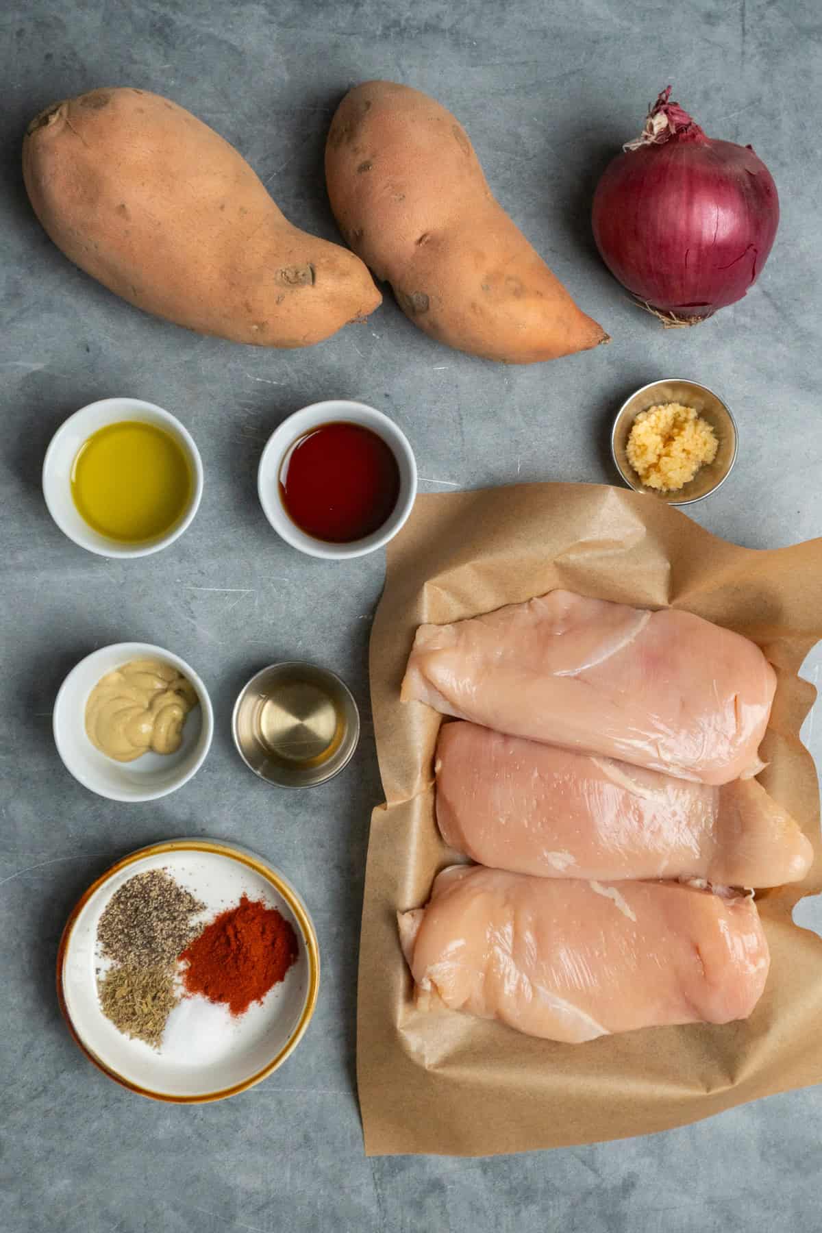 Ingredients to make chicken and sweet potatoes on a gray countertop.