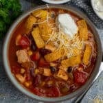 Chicken taco soup in a bowl topped with sour cream, cheese and tortilla strips.