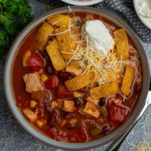 Chicken taco soup in a bowl topped with sour cream, cheese and tortilla strips.
