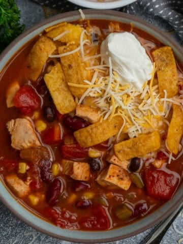 Chicken taco soup in a bowl topped with sour cream, cheese and tortilla strips.