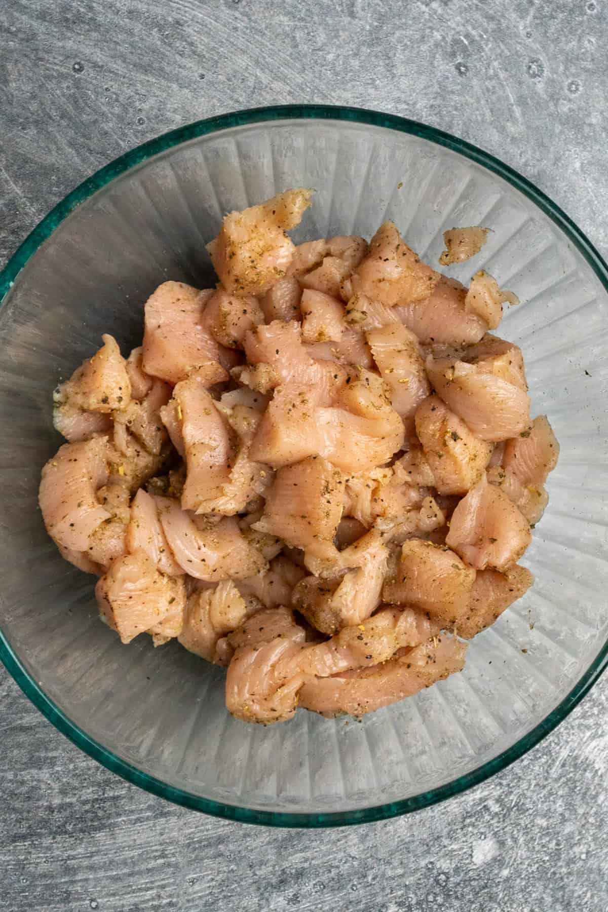Chicken cubed and seasoned in a clear bowl.