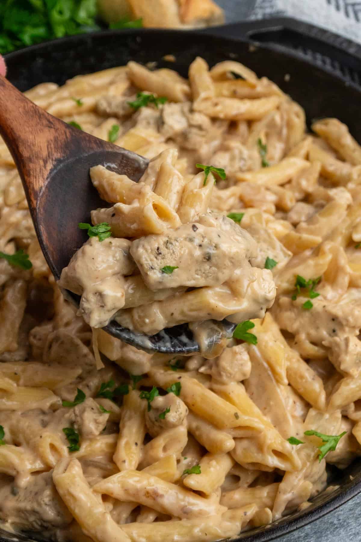 A wooden spoon holding a scoop of French onion chicken pasta.