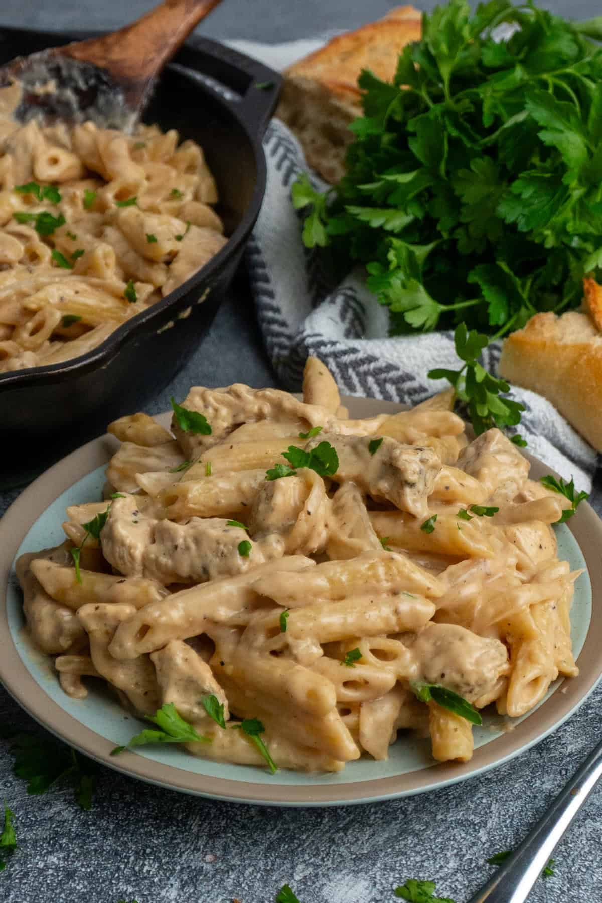 French onion chicken pasta on a plate with more in a skillet.