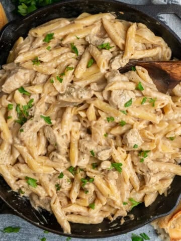 French onion chicken pasta in a cast iron skillet with a wooden spoon.