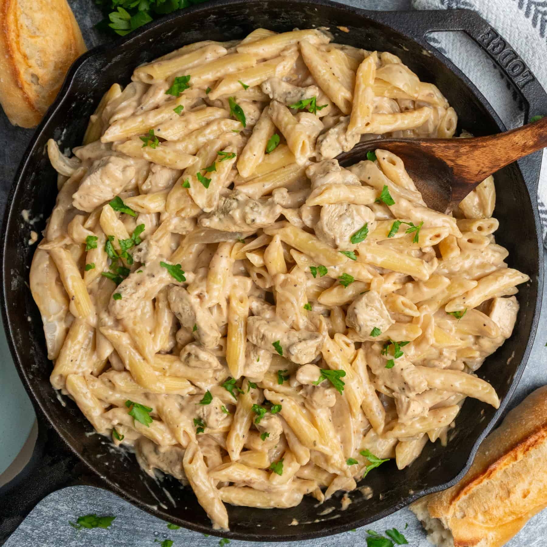French onion chicken pasta in a cast iron skillet with a wooden spoon.