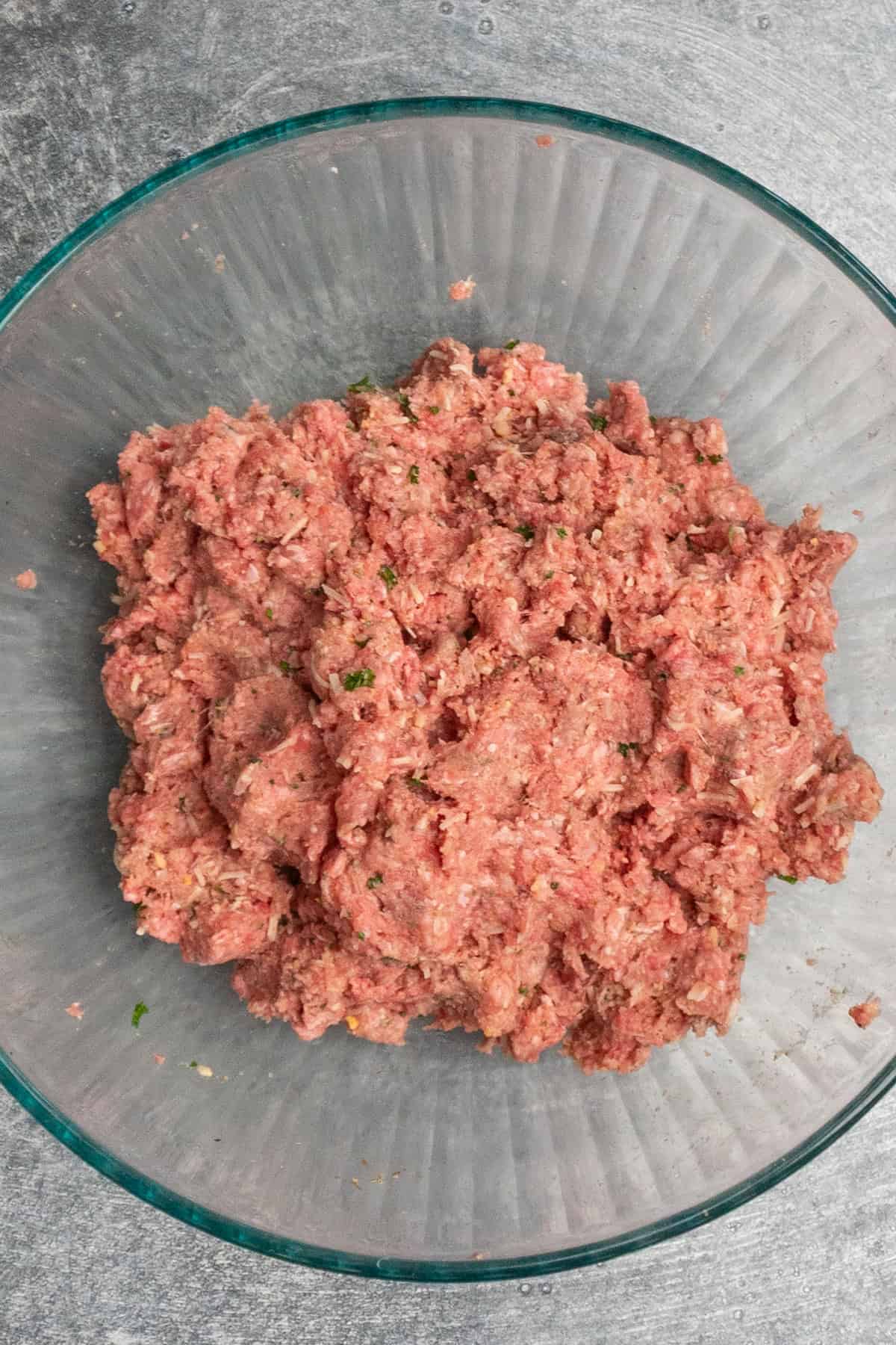 Ground beef, breadcrumbs, milk, eggs, parmesan cheese, parsley, garlic, Worcestershire sauce and seasonings mixed together in a clear bowl.