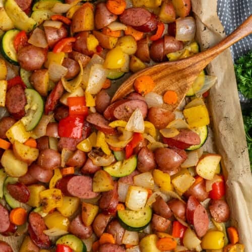 Sheet pan sausage and veggies on a baking sheet with a wooden spoon.