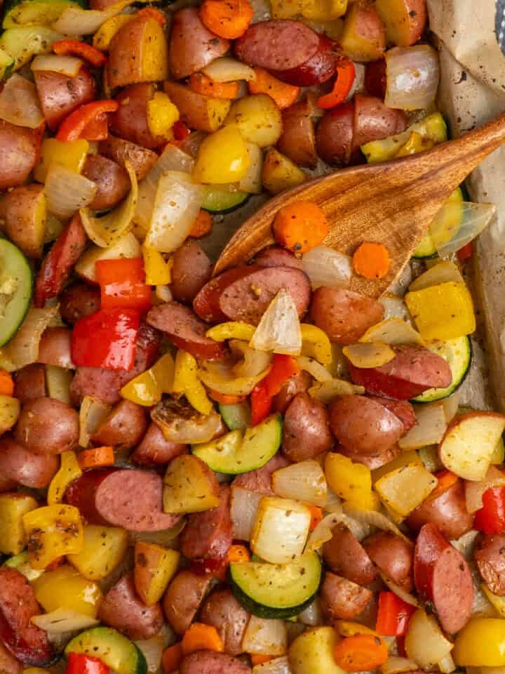 Sheet pan sausage and veggies on a baking sheet with a wooden spoon.