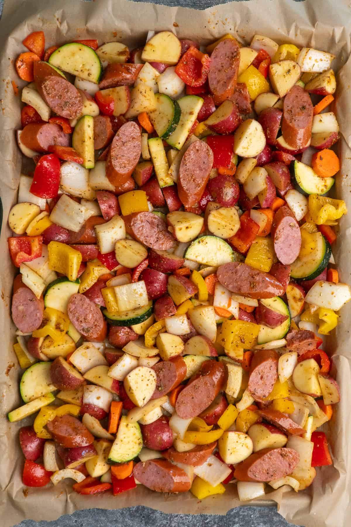 Sausage and veggies on a parchment lined baking sheet covered in glaze.