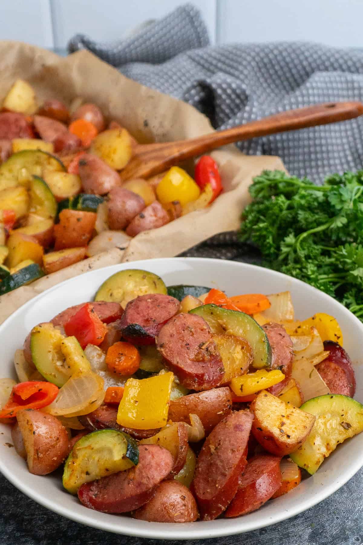 Sausage and veggies in a bowl and on a sheet pan.