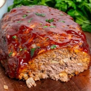 Stove Top stuffing meatloaf with a slice cut off on a wood cutting board.