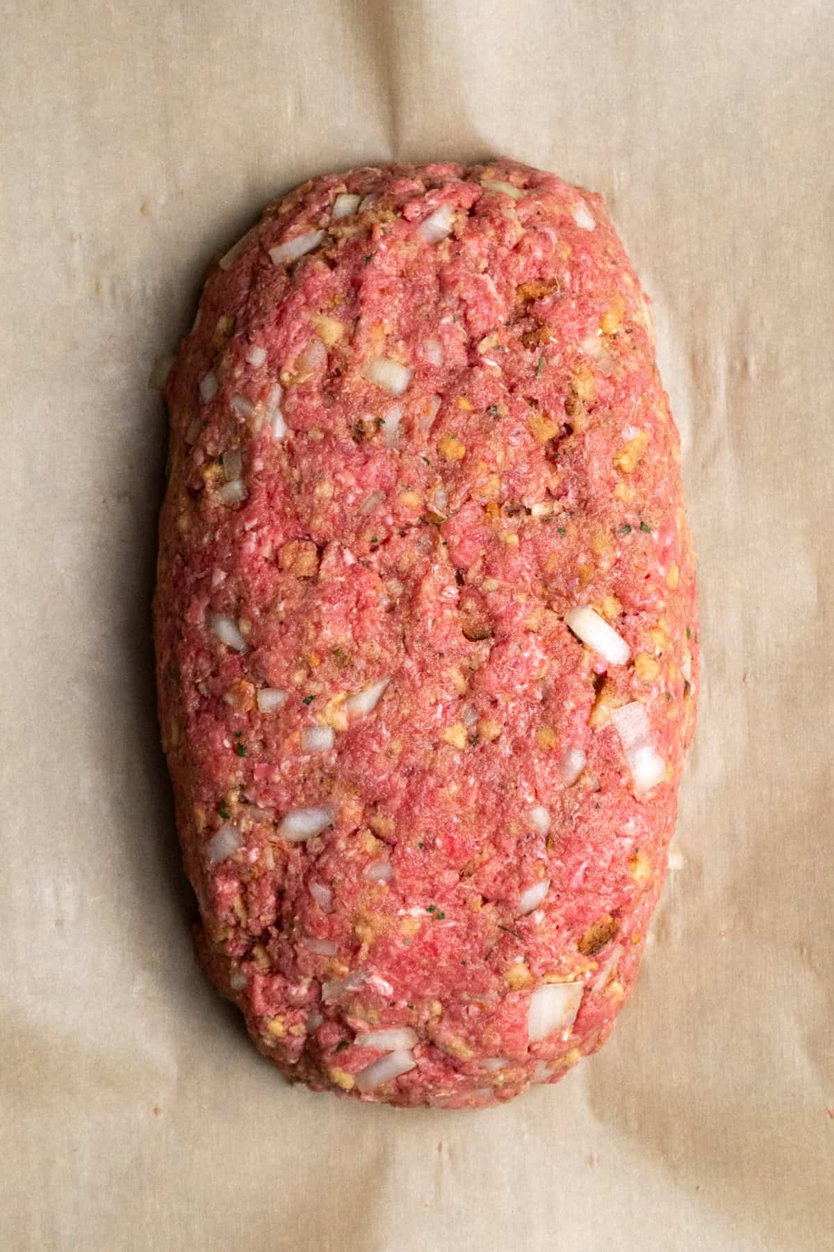 Meatloaf shaped into a loaf on a parchment lined baking sheet.