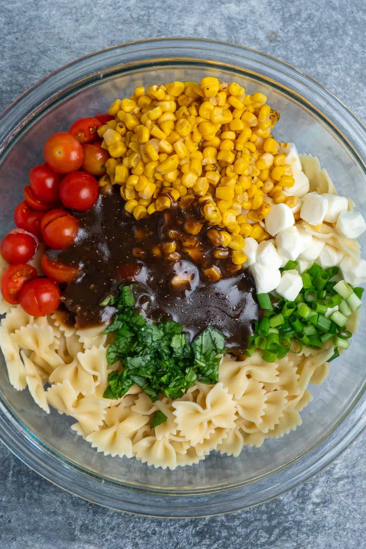 Pasta, vegetables, cheese, and dressing in a bowl ready to be mixed together.