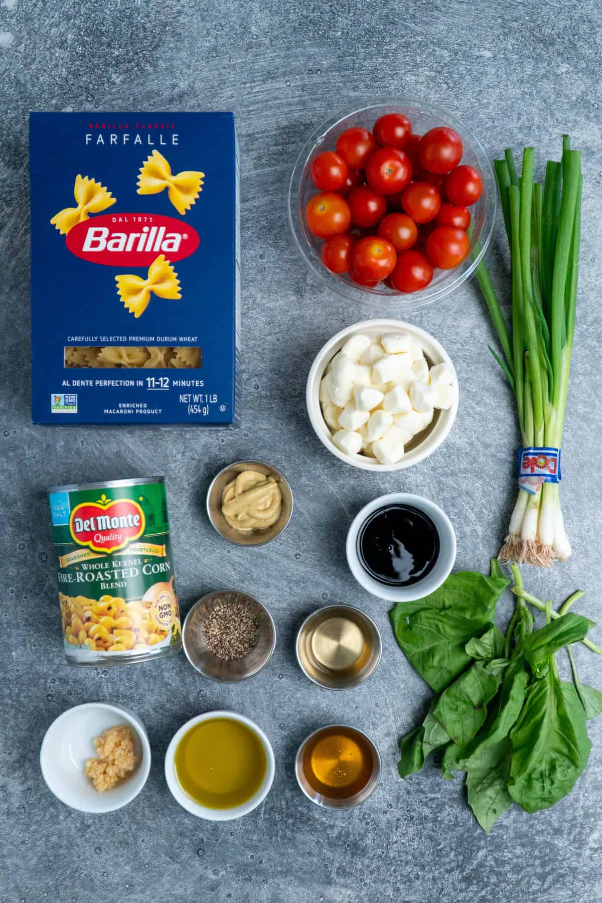 Ingredients to make caprese pasta salad on a gray stone countertop.