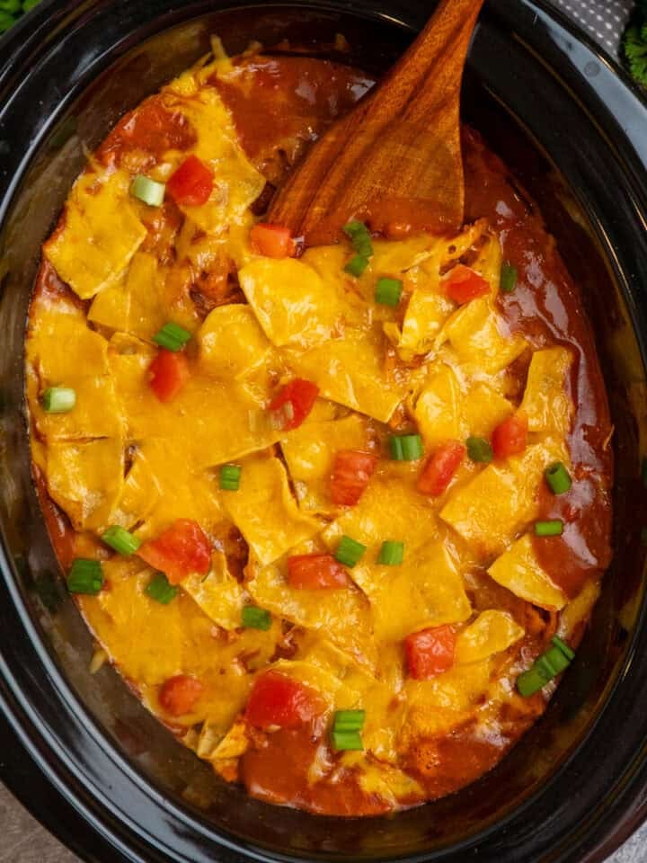 Crock Pot chicken enchilada casserole with a wooden spoon in it ready to be served.
