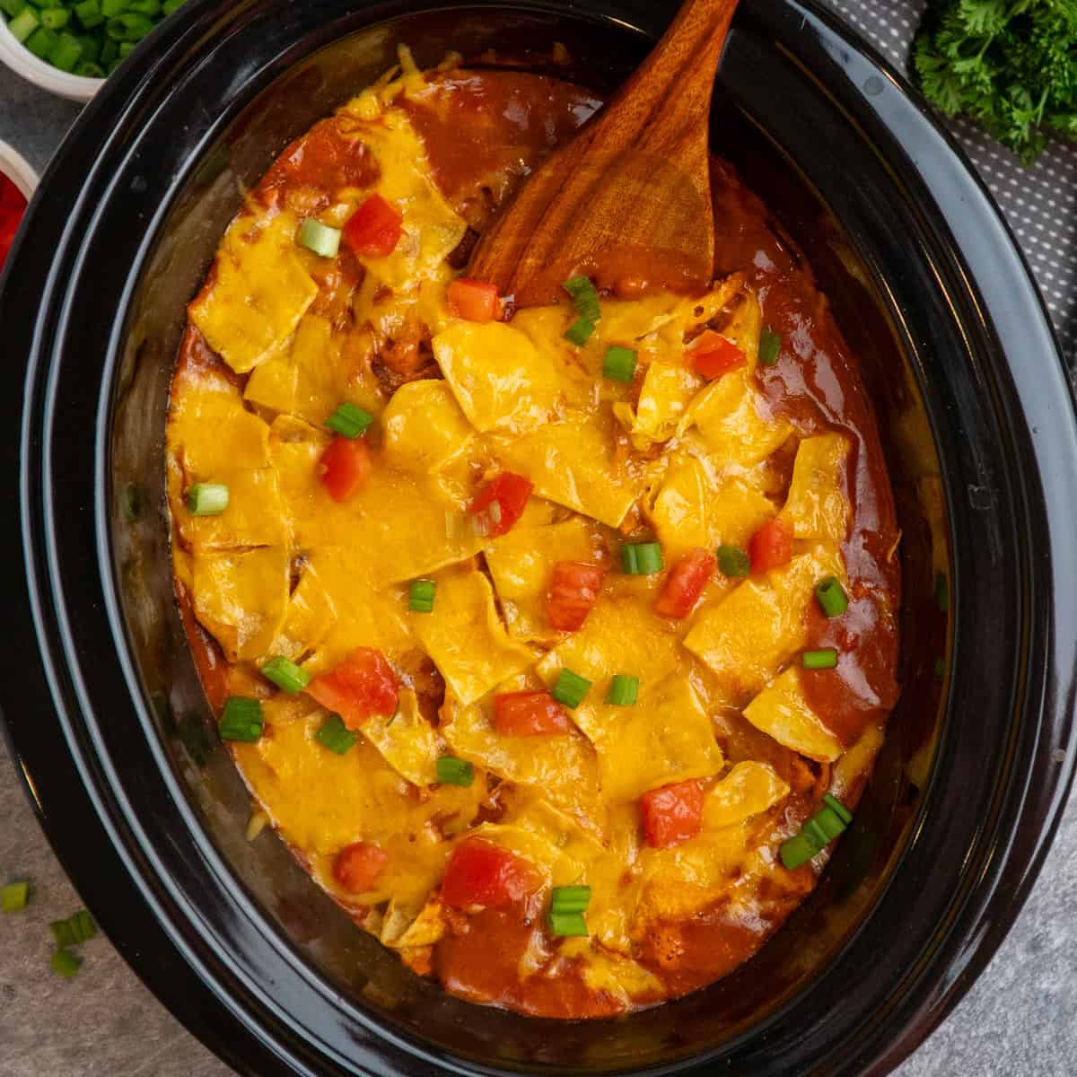 Crock Pot chicken enchilada casserole with a wooden spoon in it ready to be served.
