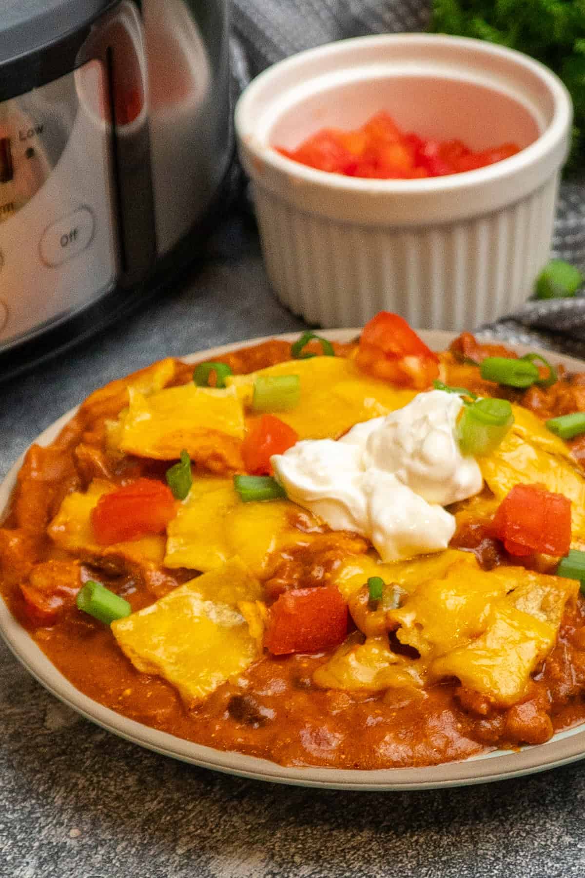 Chicken enchilada casserole on a plate and topped with sour cream, green onions and tomatoes.