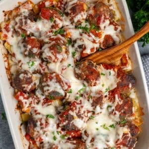 Meatball casserole in a white baking dish with a wooden spoon ready to serve.