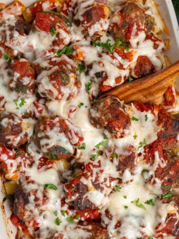 Meatball casserole in a white baking dish with a wooden spoon ready to serve.