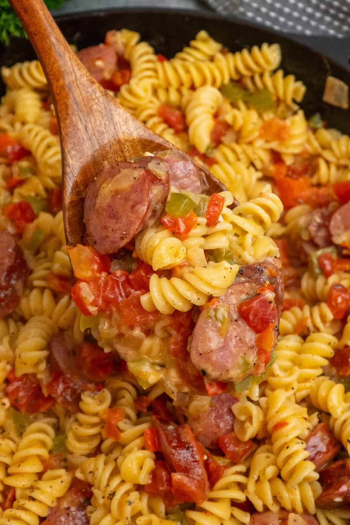 A wooden spoon holding a scoop of Rotel pasta over a skillet.