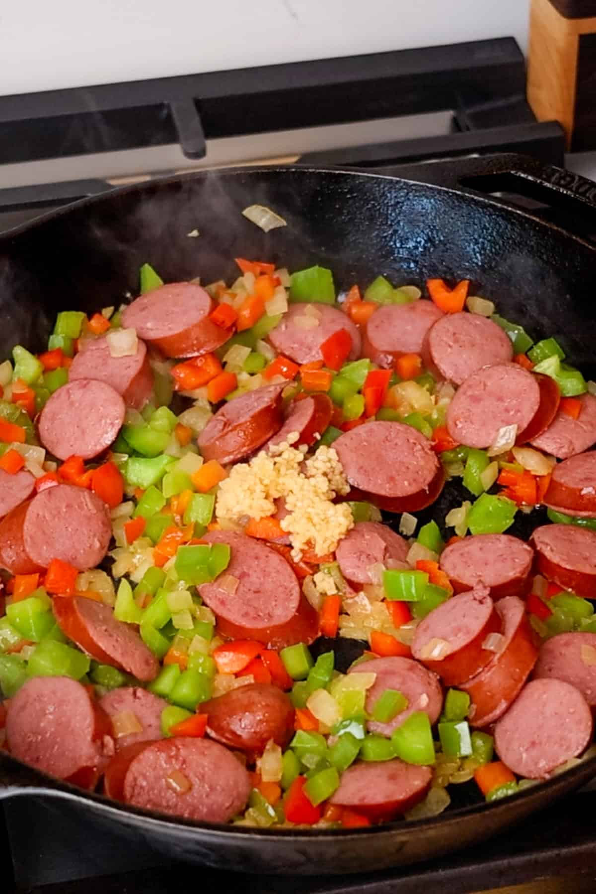 Bell peppers, onions and sausage being sauted in a cast iron skillet.