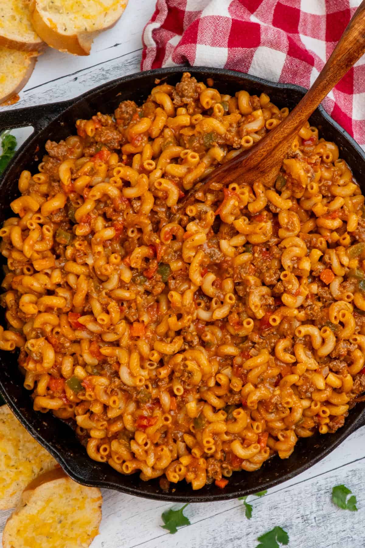 A wooden spoon mixing some American goulash in a pan.